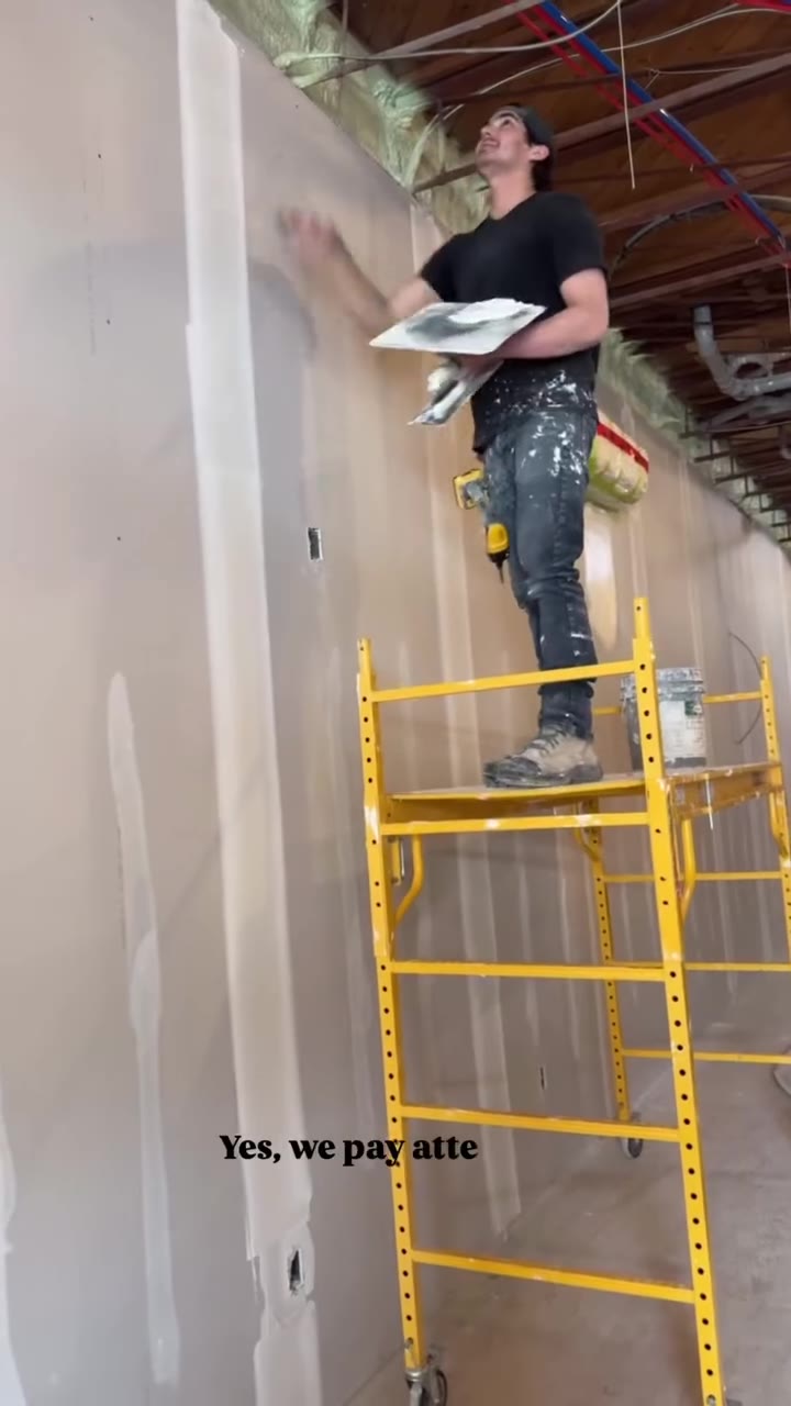 Installer working from scaffolding beside a framed wall