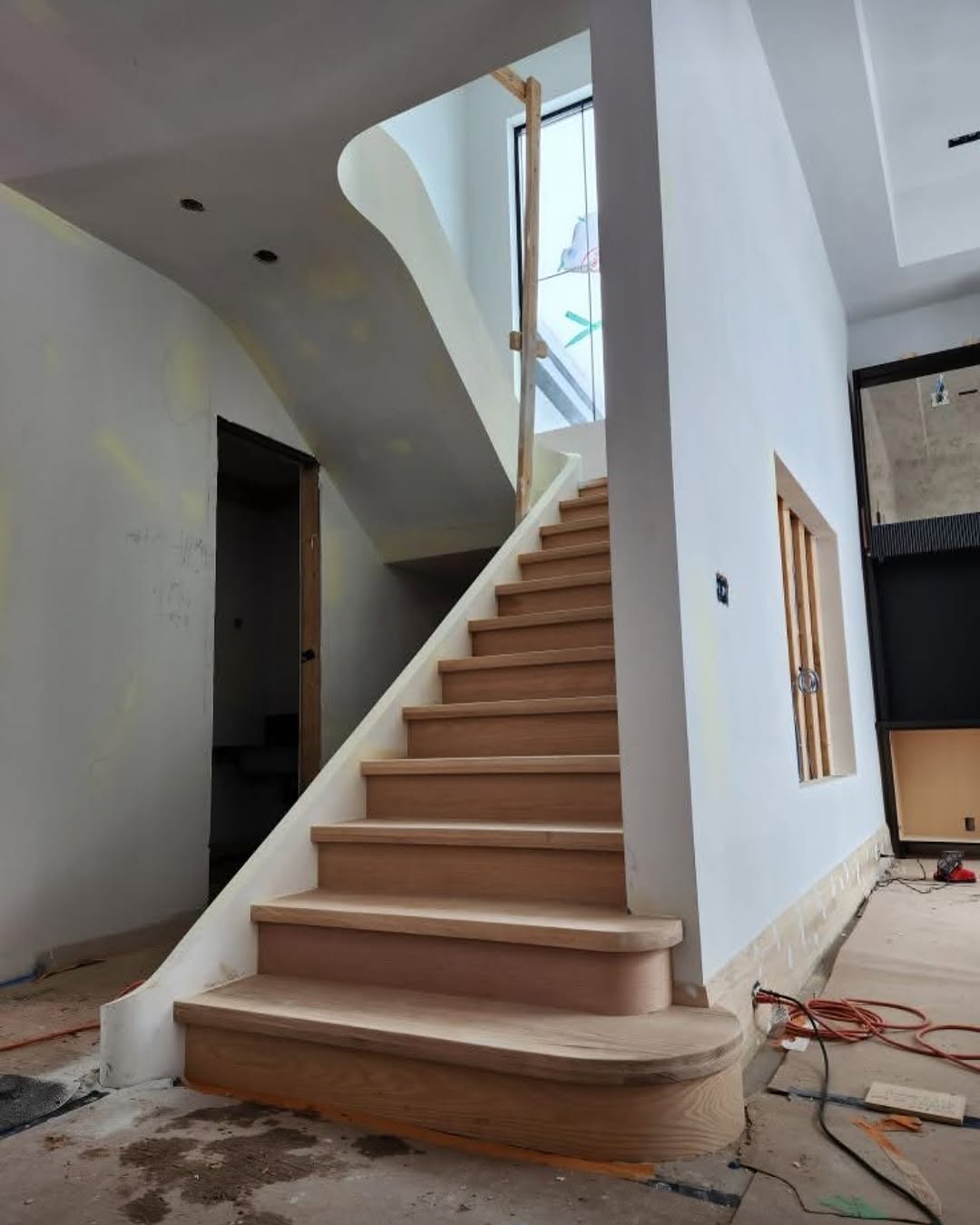 Curved oak staircase under construction in an unfinished interior